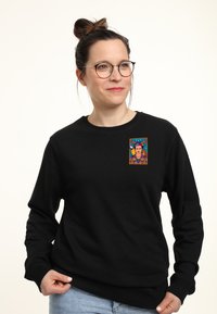 Sudadera negra de manga larga que presenta un parche gráfico colorido que representa una cara y diseños vibrantes en el área del pecho.