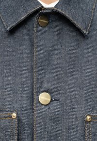 Σκούρο τζιν μπουφάν με μυτερό γιακά, χρυσά κουμπιά υλικού, αντίθετη ραφή και τσεπάκι. Η υφή είναι ανθεκτική και υφασμένη.