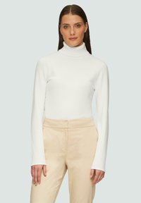 Haut à col roulé blanc avec des manches longues, texture lisse, design ajusté. Associé à un pantalon taille haute beige, style minimaliste.