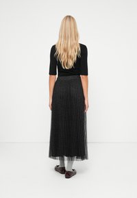 Svart, plisserad maxikjol med ett strukturerat mönster, genomskinlig överdrag, elastisk midja och slätt foder; matchad med grå strumpor och burgundy skor.