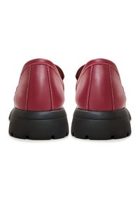 Scarpe in pelle rossa con una forma arrotondata, dotate di suole in gomma nera e cuciture visibili sul tallone per un ulteriore tocco di dettaglio.