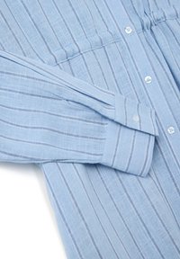Camicia azzurro chiaro in tessuto testurizzato, con righe verticali di un blu più scuro, polsini con bottoni e un design dal taglio rilassato.