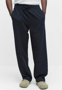 Marinblå randiga byxor med vida ben, dragsko i midjan och mjuk textur. Har vertikala vita ränder som detalj.