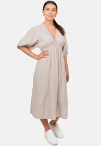 Beige textuur midi-jurk met een V-hals, pofmouwen en een geraffineerde taille, gestyled met witte sneakers.
