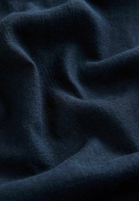 Tissu bleu marine foncé avec des plis doux et un tissage fin texturé, montrant un ombrage doux et des détails de surface lisses.