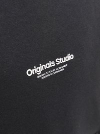 Tissu noir avec un logo blanc proéminent portant la mention "Originals Studio" et un texte en dessous indiquant la marque et l'origine du design.