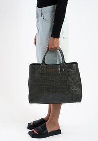 Donkergroen handtas met krokodillenstructuur, twee handvatten, rechthoekige vorm, goudkleurige hardware en een gladde, glanzende afwerking.