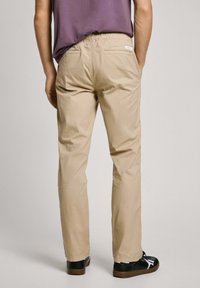 Pantalones beiges de pierna recta con cintura elástica, que cuentan con dos bolsillos traseros y una textura de tela suave. Combinados con calzado negro.