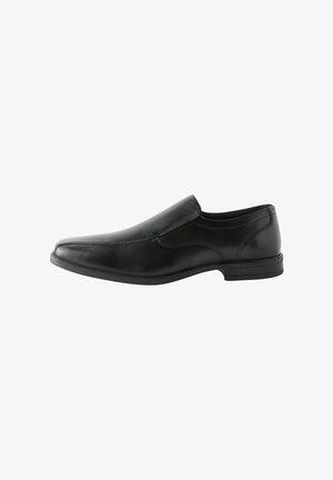 Scarpa slip-on in pelle nera con texture liscia, punta leggermente affusolata, tacco basso e dettagli di cucitura minimalista lungo la tomaia.