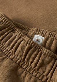 Brązowa tkanina o prążkowanej fakturze posiada elastyczny pas i guzik z małą pętelką. Widok z bliska ukazujący szczegóły i szwy.