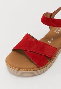 Sandale en daim rouge avec des brides entrecroisées, une semelle intérieure rembourrée marron et une semelle plateforme texturée de couleur claire.
