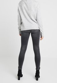 Grijze gebreide trui en donkergrijze skinny jeans met enkellaarsjes. De jeans hebben een gladde textuur en een slim fit ontwerp.