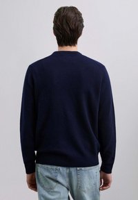 Maglione lavorato a maglia blu navy con collo a girocollo, polsini e orlo a costine, indossato con jeans in denim azzurro, vista da dietro.