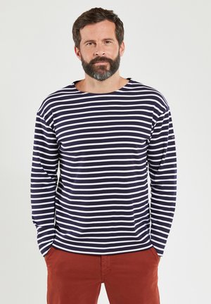 Langärmliges gestreiftes Shirt in Navy und Weiß, lockere Passform mit Rundhalsausschnitt und gerippten Bündchen, kombiniert mit rostfarbenen Hosen.