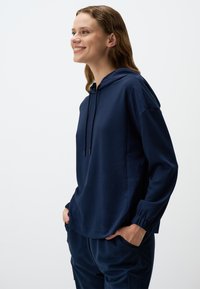 Felpa blu navy con cappuccio, dotata di coulisse, maniche lunghe con polsini elasticizzati e vestibilità morbida. Realizzata in un tessuto morbido e liscio.