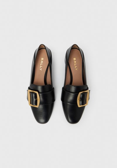 Μαύρα δερμάτινα φλατ παπούτσια με μυτερή μύτη και φαρδιά λωρίδα με χρυσή αγκράφα. Το εσωτερικό έχει ταμπά δερμάτινη επένδυση με το λογότυπο της μάρκας.