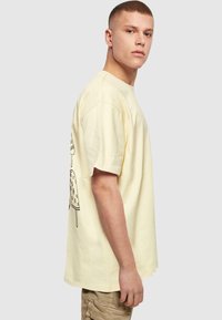 Gul bomulds t-shirt med korte ærmer, med et sort grafisk motiv af en isvaffel på ryggen. Løs pasform og rund halsudskæring.