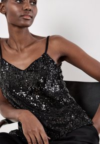 Schwarzes Pailletten-Camisole mit dünnen Trägern und V-Ausschnitt. Der Stoff hat ein glänzendes, strukturiertes Aussehen durch überlappende Pailletten.