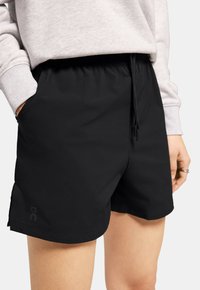 Schwarze Sportshorts mit einem elastischen Bund, Zugband und Seitentaschen. Glatte Textur, Logodetail am Saum.
