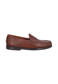 Mocasin de cuero marrón con una parte superior texturizada, acentos de costura y una suela de goma. Presenta un emblema lateral y un leve tacón.