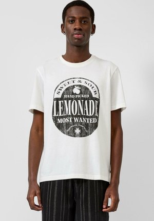 Jonge man draagt wit T-shirt met zwarte vintage-stijl "Sweet & Sour Hand Picked Lemonade Most Wanted" tekst en grafische elementen.