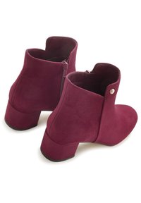 Burgunderfarbene Ankle Boots mit samtiger Textur, niedrigen Blockabsätzen, seitlichen Reißverschlüssen und einem kleinen metallischen Akzent.