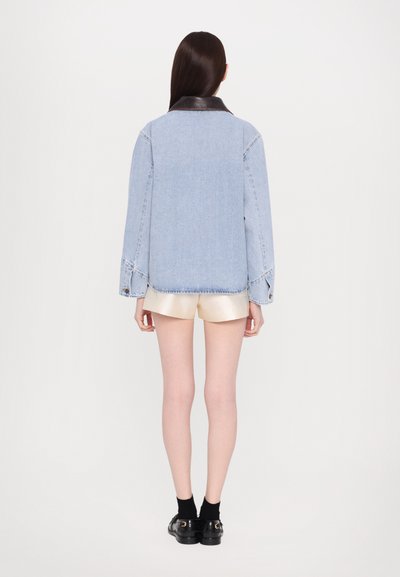 Denimjack met een zwarte leren kraag, lange mouwen en manchetten; gecombineerd met glanzende crèmekleurige shorts. Achteraanzicht tegen een effen achtergrond.