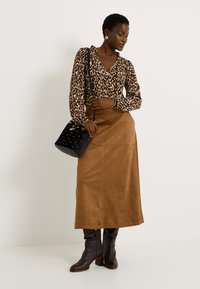 Blusa de estampado de leopardo con escote con volantes, falda larga de ante marrón, bolso negro con tachuelas y botas de cuero marrón hasta la rodilla.