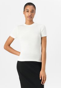 Hvid kortærmet striktrøje med teksturerede striber, rund halsudskæring og tætsiddende design. Parret med en sort nederdel, der skaber et to-farvet look.