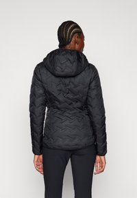 Svart dunjakke med hette, med en quiltet zigzag-mønster og innsnørt midje, laget med et glatt, vannavstøtende yttermateriale.