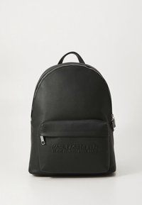 Črni usnjeni nahrbtnik z zaobljeno obliko, ki ima sprednji žep z zadrgo, vtisnjen logotip in kontrastne poudarke zadrge.