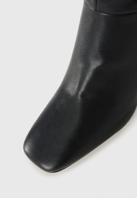 Stivale ankle in pelle nera con punta quadrata e superficie liscia, leggermente pieghettata, su sfondo bianco.