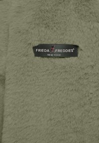 Tkanina z sztucznego futra w oliwkowo-zielonym kolorze o miękkiej fakturze; posiada czarną metkę z napisem "FRIEDA FREDDIES NEW YORK" w białym kolorze oraz sylwetką psa.