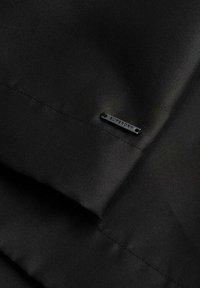 Tissu noir avec une texture lisse, comportant une petite étiquette noire "SUPERDRY", mettant en avant un design épuré et simple.