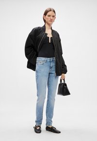 Μαύρο μπουφάν, μαύρο μπλουζάκι, ανοιχτό μπλε τζιν, μαύρη τσάντα και μαύρα παπούτσια. Το σύνολο διαθέτει χαλαρή εφαρμογή και casual στυλ.