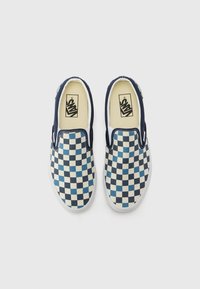 Zapatos slip-on de cuadros azul y crema con suela de goma blanca y acentos laterales elásticos, que cuentan con un logo en la plantilla.