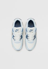 Sneakerii Nike Air Max au o parte superioară albă și albastră deschisă, cu accente bleumarin, textură de piele netedă, șireturi plate și o guler moale.
