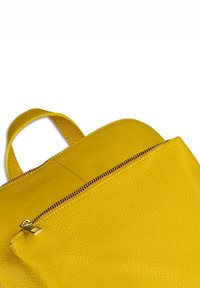 Geel lederen rugzak met een gestructureerde afwerking, voorzien van een ritsvak en een ronde bovenhandgreep. Glad afgewerkte randen en metalen ritsdetails.