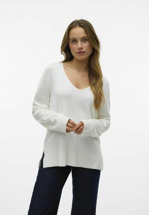 Maglione bianco a maglia con scollatura a V, maniche lunghe e spacchi ai lati. Texture morbida, vestibilità comoda, abbinato a pantaloni in denim scuro.