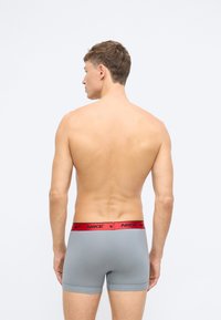 Šedé boxerky s červeným elastickým pásom, na ktorom je logo Nike. Dizajn je priliehavý a má hladkú textúru.