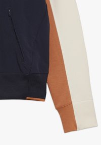 Pullover jacket featuring a navy body with contrast sleeves in orange and cream, textured ribbed cuffs, and a zippered pocket on the side.