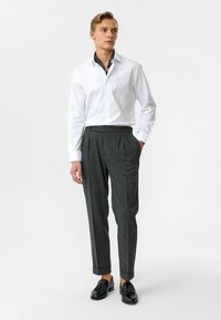 Witte overhemd met een patroon op de kraag, gecombineerd met donker gestreepte broek en zwarte instappers. Schone lijnen en een pasvorm op maat.