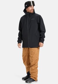 Black zip-up jacket with hood, paired with brown pants. The jacket features a subtle logo and side pockets, while the pants have cargo-style pockets.