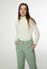 Weißer gerippter Rollkragenpullover mit langen Ärmeln, kombiniert mit mintgrünen Hosen mit Fronttaschen und Knopfverschluss.