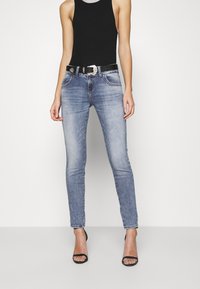 Smaljeans i lyseblå denim med en falmet finish, kombinert med en svart tanktopp og et svart belte med en metallisk spenne.