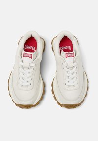 White sneakers with a textured leather upper, lace closure, and contrasting red inner lining. Features a rugged brown rubber outsole.