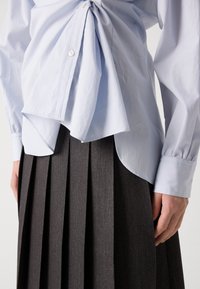 Chemise bleu clair à boutons avec un détail froncé à l'avant, associée à une jupe plissée gris foncé. Texture lisse et couleurs contrastées.