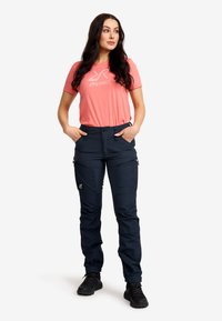 Kortärmad korallfärgad t-shirt med en ljusgrå logotyp, kombinerad med marinblå cargo-byxor med dragkedjefickor och en figurnära design, kompletterad med svarta vandringsskor.