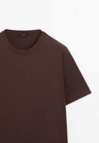 T-shirt marrone a maniche corte realizzato in morbido cotone, con scollatura tonda e design minimalista, caratterizzato da una texture liscia e dettagli di cucitura discreti.