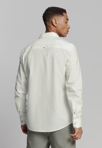 Lichtgekleurde button-up shirt van gestructureerde stof. Heeft lange mouwen, een klassieke kraag en een enkele knoopdetail aan de achterkant.